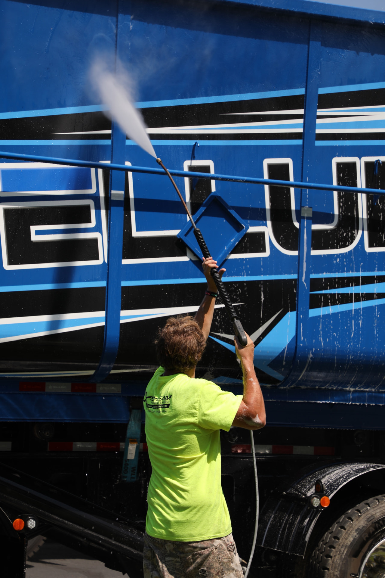 Worker in a yellow XStream jacket pressure washing a blue semi trailer